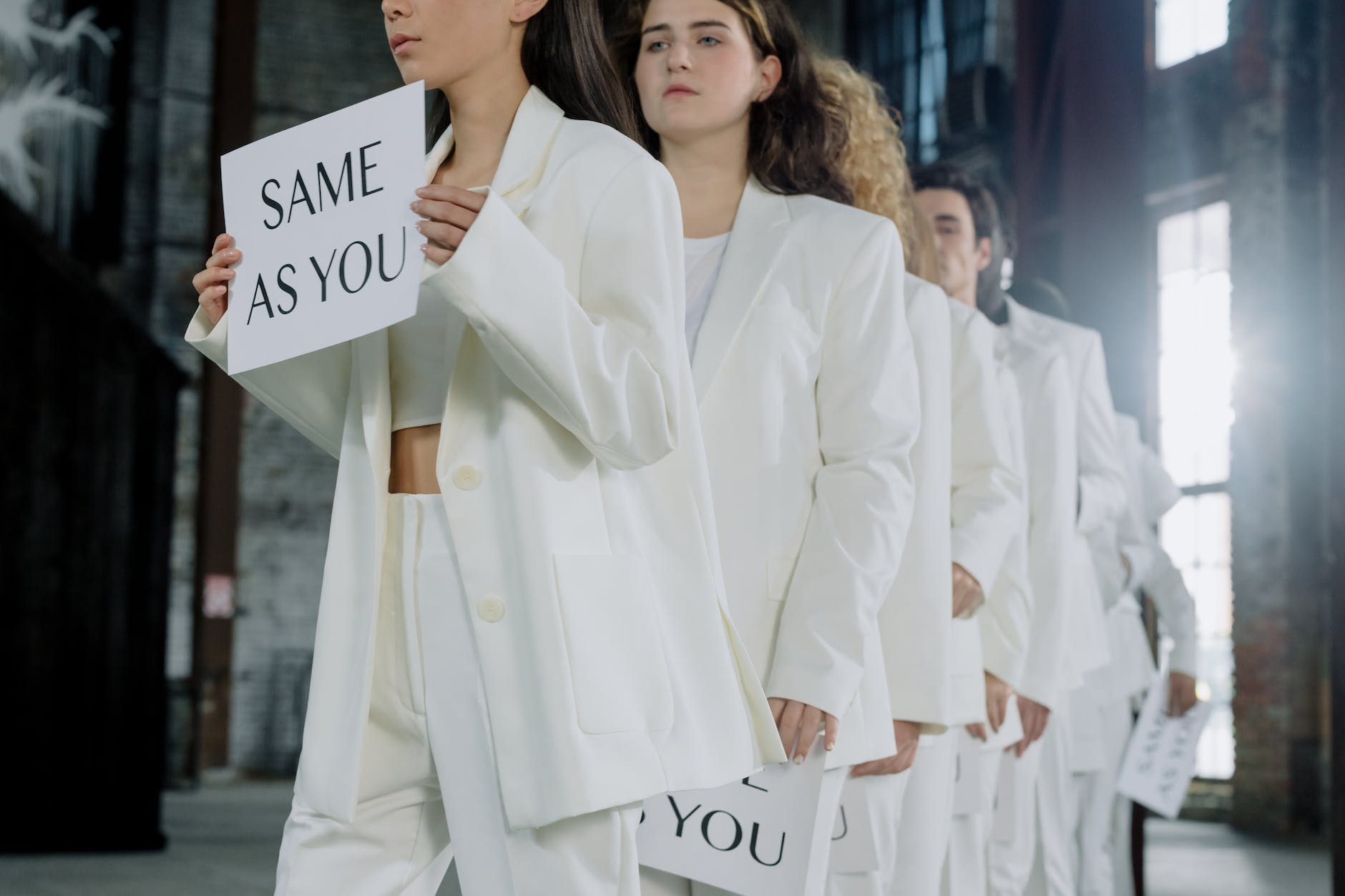 Have you heard of a line? People in white standing in a line holding signs that say: Same as you. 